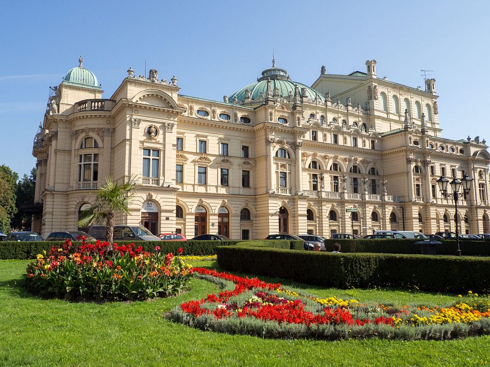 A large, ornate building in Krakow, Poland: white with about 4 stories, and ornate decorations around the windows. A green dome on top. 