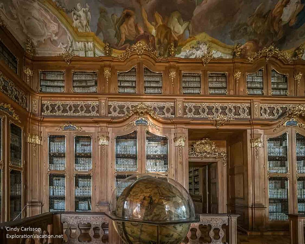 The library at Kroměříž: glass-fronted built-in wooden cabinets, richly decorated and full of books, an antique globe on a table, and a Baroque painted ceiling.