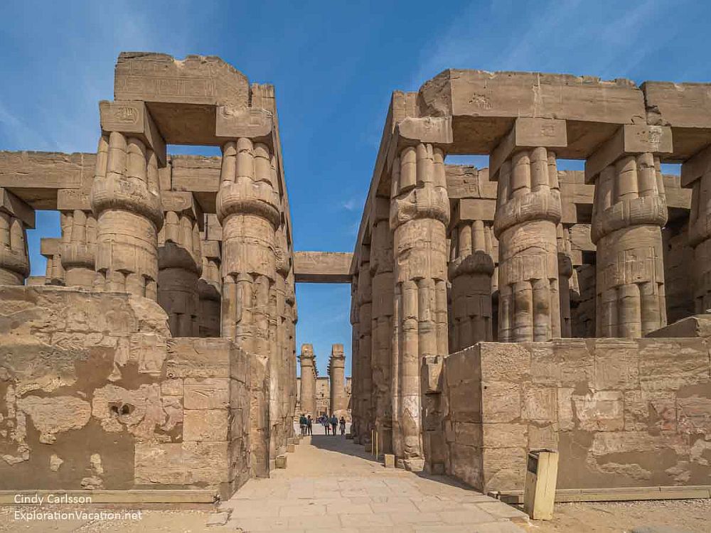 Looking between rows of large columns, each looking like a bundle of smaller columns. People are visible far down the row, looking very small.