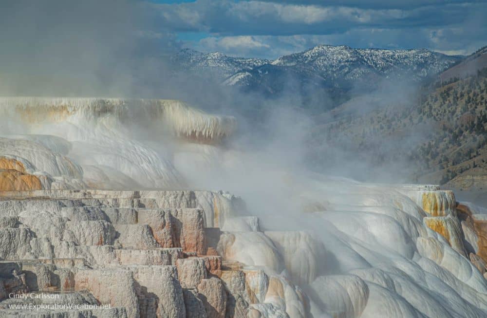 steam rises from a slope of hardened minerals in shades of white and red.