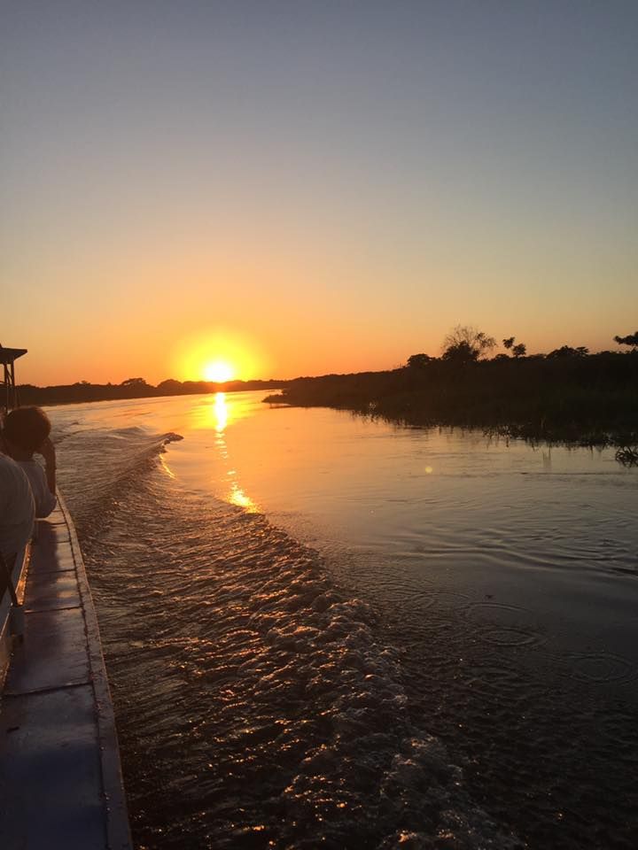 Looking behind a moving boat at the sunset down the river. The water is smooth except where the boat's wake stirs it up. 