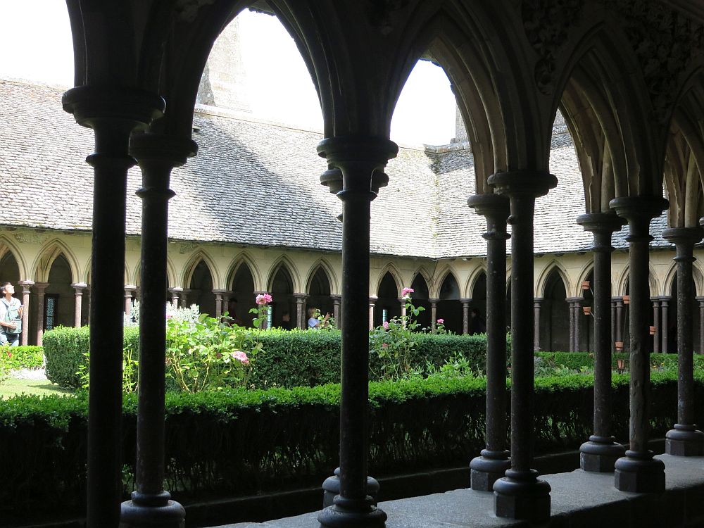 Delicate pillars support gothic arches: a double row in the foreground, and a view across a garden to the same arches on the opposite side.