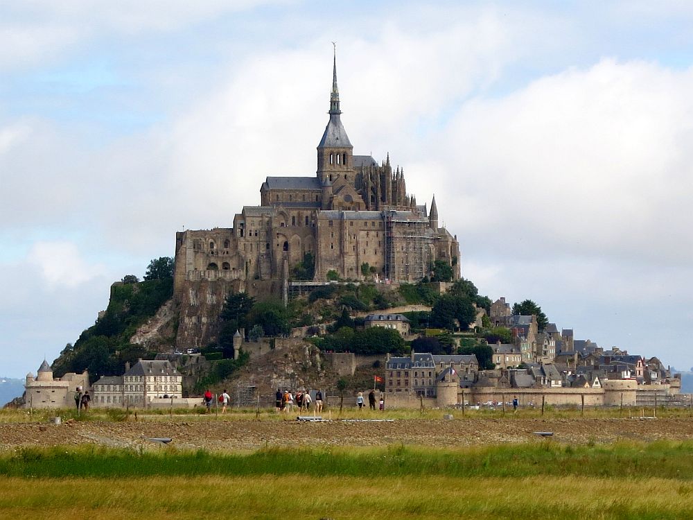 Mont-Saint-Michel appears as a pile of stone structures up a hill, forming a conical shape with a recognizably Gothic church spire at the top.
