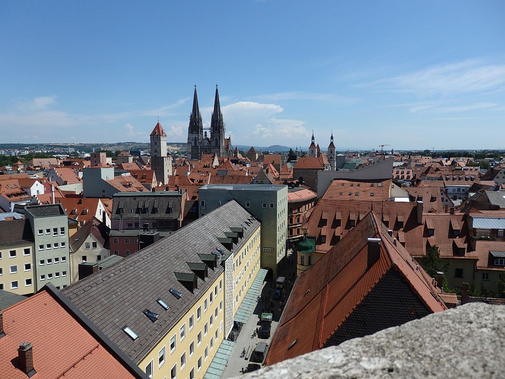 View over Regensburg - red roofs, pastel-walled buildings - with the two spires of the cathedral in the distance.