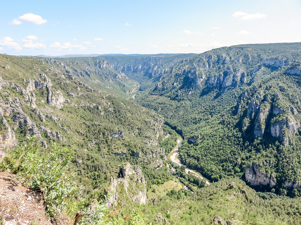 A view into a wide gorge - a river cut through the bottom, and low shrubs or grasses along both banks and up the sides of the gorge.