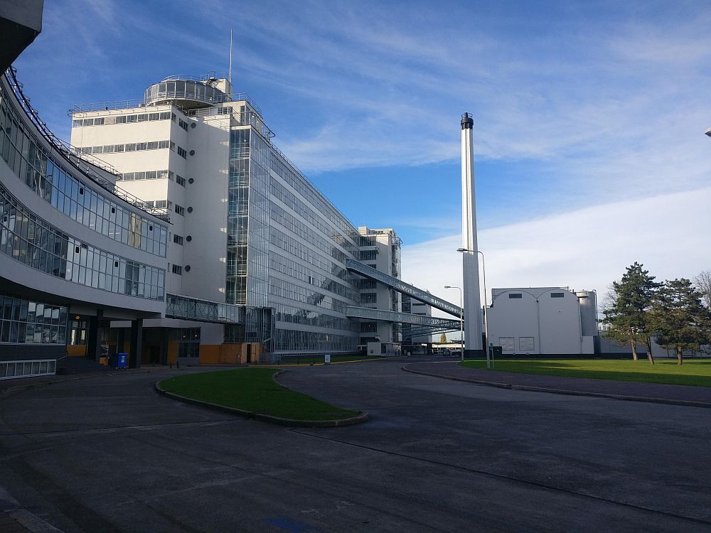 A view of the Van Nellefabriek from the side: the building is white with rows of big windows, closely set, on all 8-9 floors. 