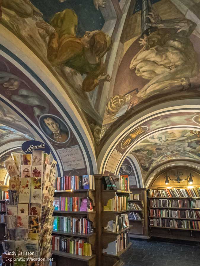 In Vilnius, and interior shot of the Littera bookshop: a column, enclosed by bookshelves at its base, curves into ribs on all four sides. Between the ribs, the ceiling is painted in baroque style.