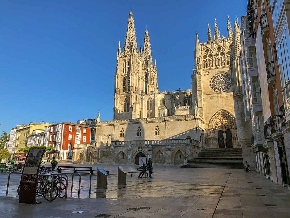 Exterior of the cathedral as seen from the plaza outside. The entrance is on the right in this view, with a highly carved gothic arch over the double door and a square tower with rose window above the door. At the left-hand end of the cathedral are two spires, square except for the topmost sections, which are pointed and very lacy.