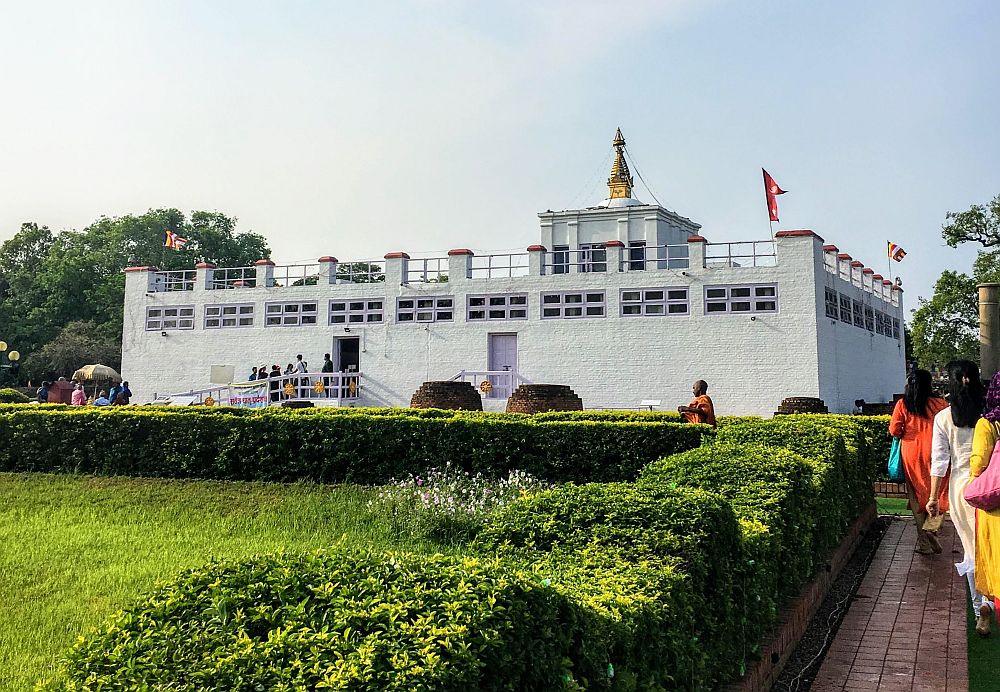 In Lumbini, Nepal, a long white building with a railing around the roof and flags on the corners.