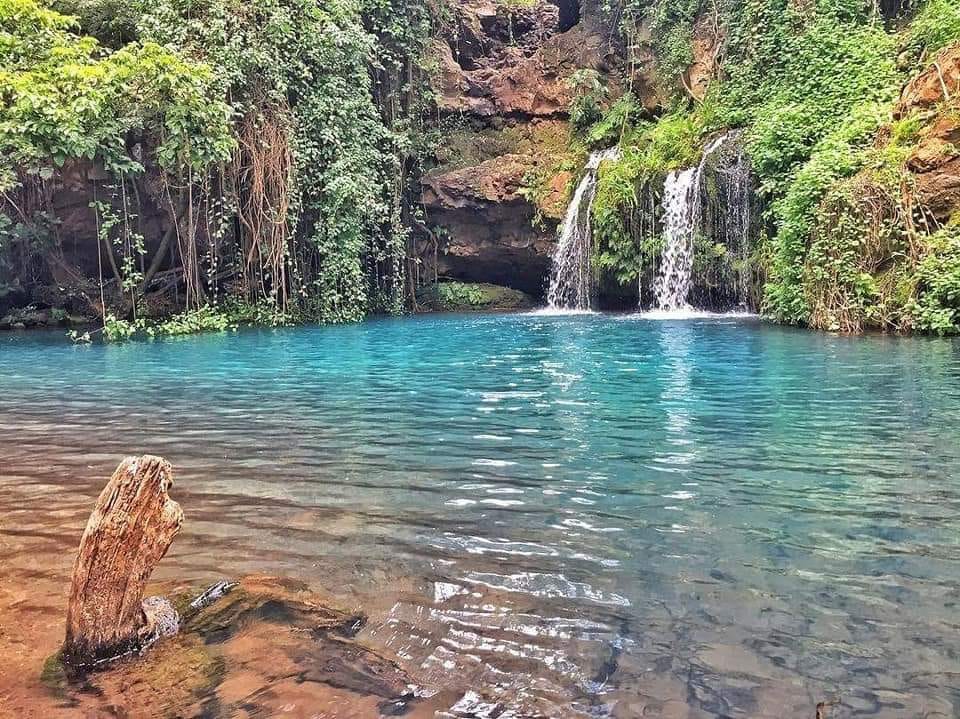 A natural pool in the forest of Ngare Ndare: blue water, greenery around it, with 2 small waterfalls tumbling into it.