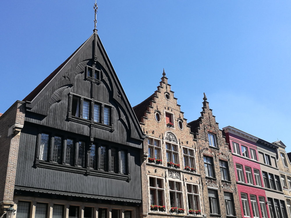 A row of buildings in the Historic Center of Brugge: the nearest 3 have pointed roofs, two of them with step gables. The other two that are visible have a flat roof.