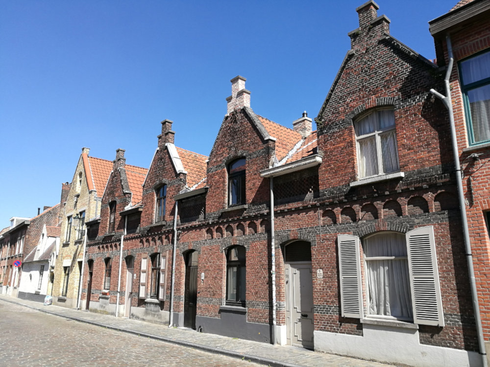 A row of modest residences in Brugge in red brick, each two stories tall, with just one door and one window on the ground floor and one window above under the peaked roofs. 