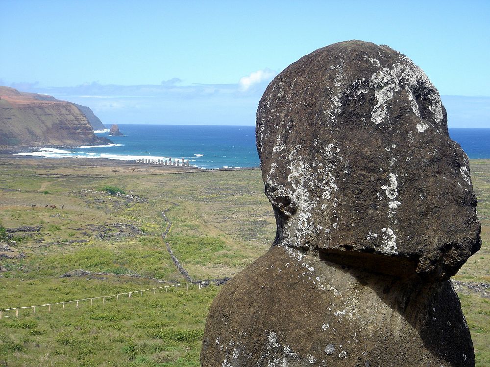 A close-up of one of the heads at Rapa Nui National Park: simple and quite eroded. Beyond that an empty, grass-covered landscape and the sea beyond.