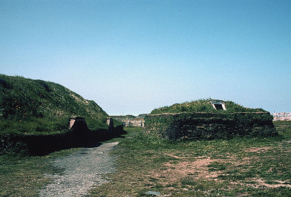 A reconstructed sod house has straight walls and a rounded roof.