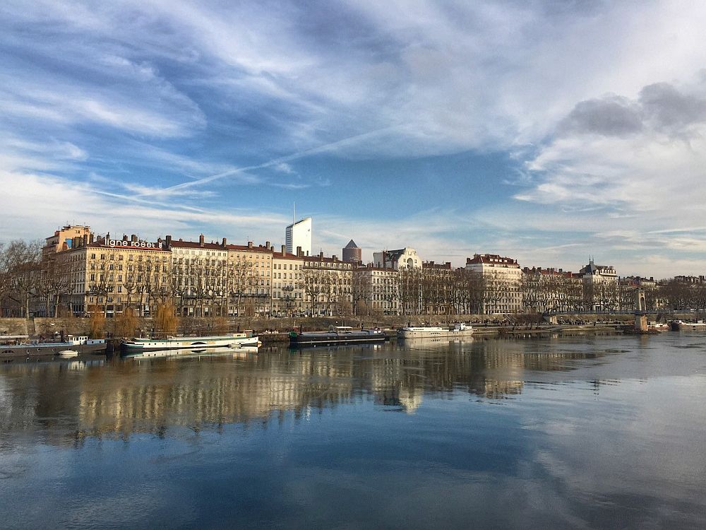 View from the river in Lyon of a row of elegant apartment houses along the river, with a few barges moored along the riverside.