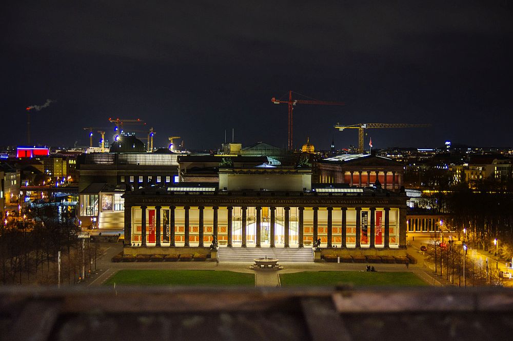 A view from above at night: the building is low with a row of very tall pillars along the front forming an open gallery along the front of the building.