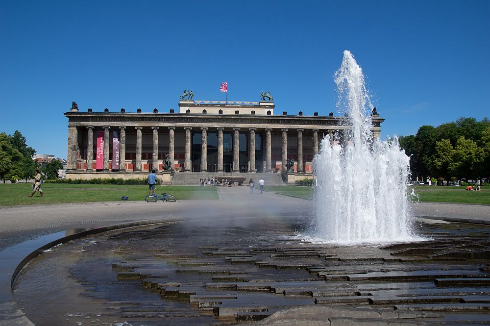 A long building with a row of columns all along the front like a Greek temple. In front of it, a fountain.