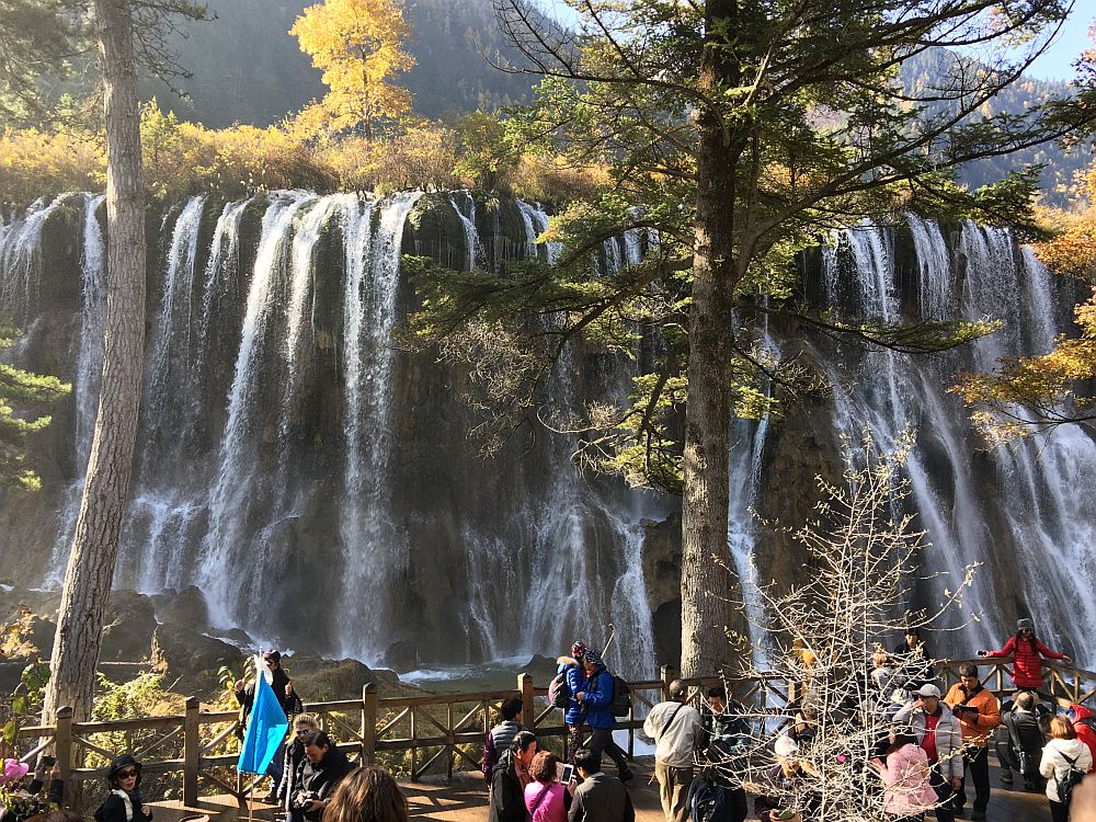 People at the bottom of the photo look up at the large waterfall behind them which fills the rest of the picture.