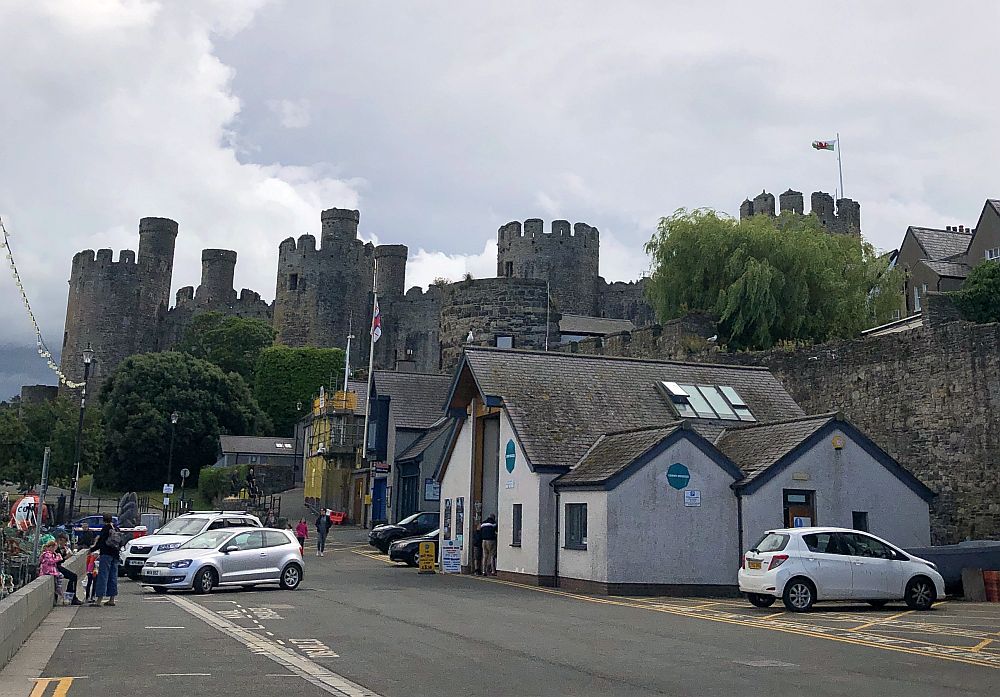 Houses and shops in the foreground, the castle rises above them on a hill in the background: stone walls, round towers with crenellations around the top.