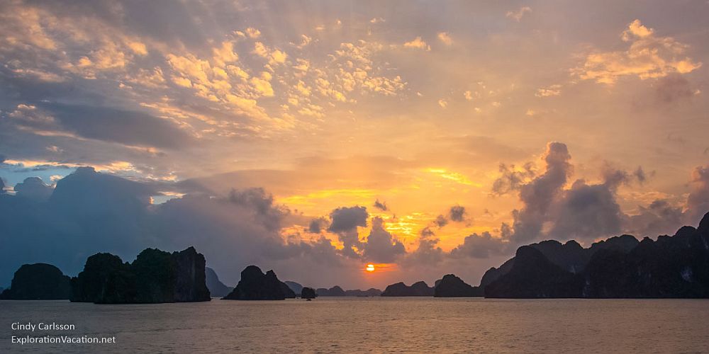 A sunset over a calm sea with a scattering of rocky islands jutting up, sillhouetted.