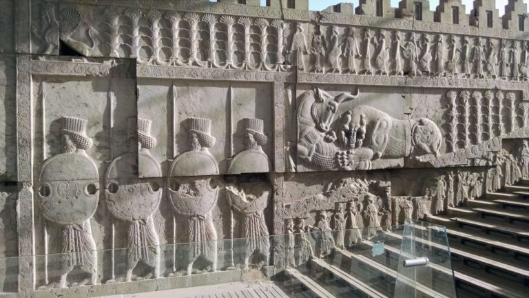 Carvings on a wall depict soldiers and a hunt.