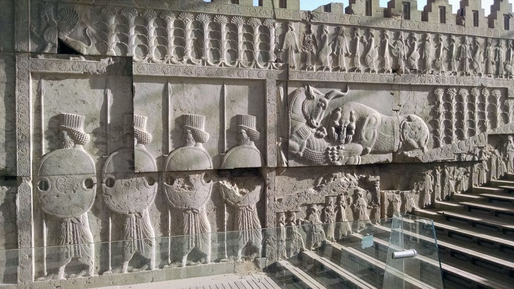 A panel of well-preserved bas-reliefs at Persepolis show a row of soldiers holding shields, a horse, and many more smaller figures of people.