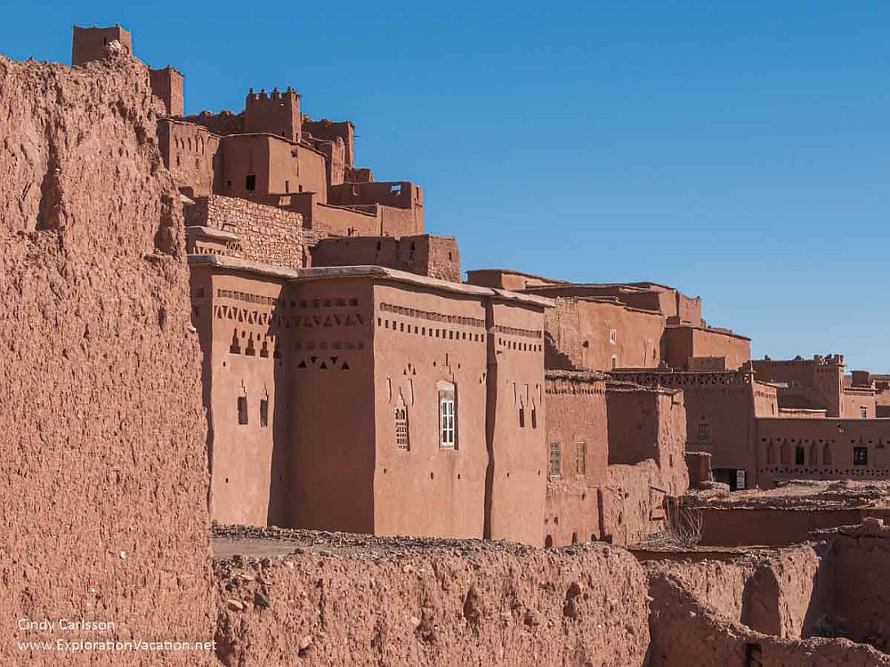 A detail of a few of the buildings: red earthen walls, very rectangular facades with few windows. Buildings are set right up next to each other.