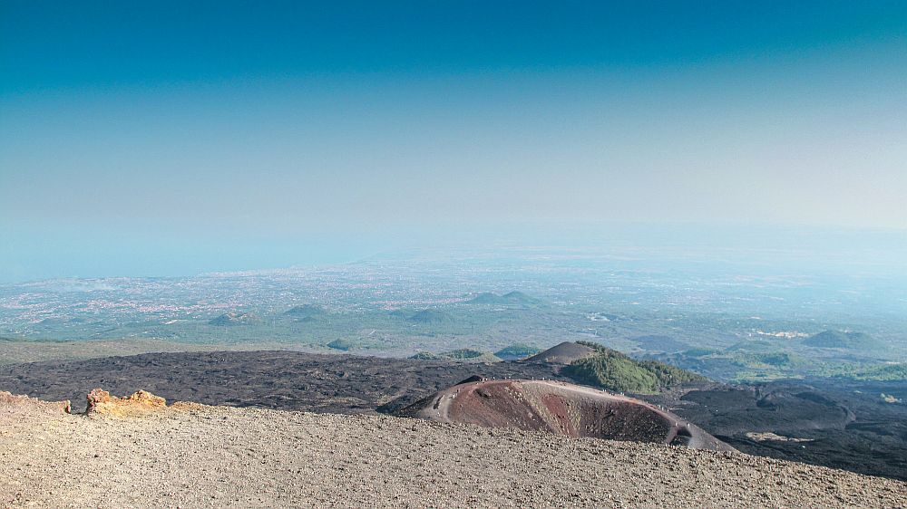 View from the Mount Etna volcano: a crater nearby and a very big view that disappears into the haze beyond that.