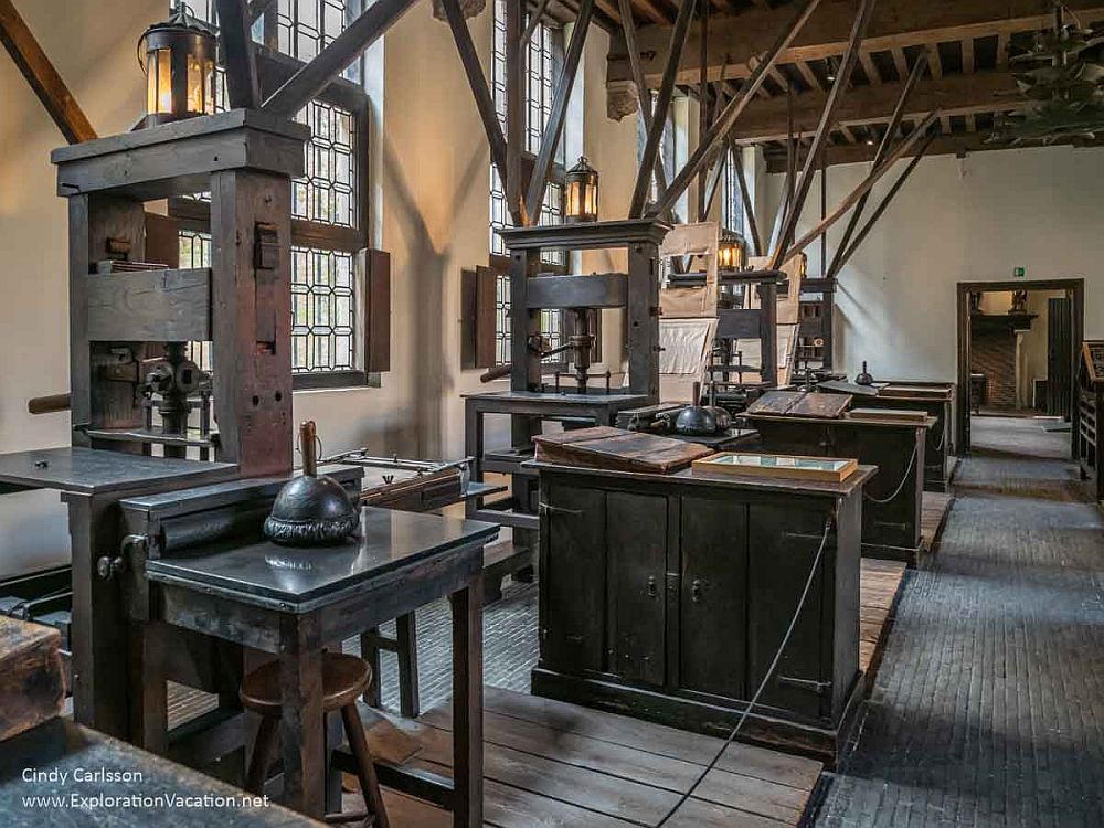 A view of the print shop in the Plantin-Moretus Museum: four printing presses in a row along a wall, with a work table next to each one.