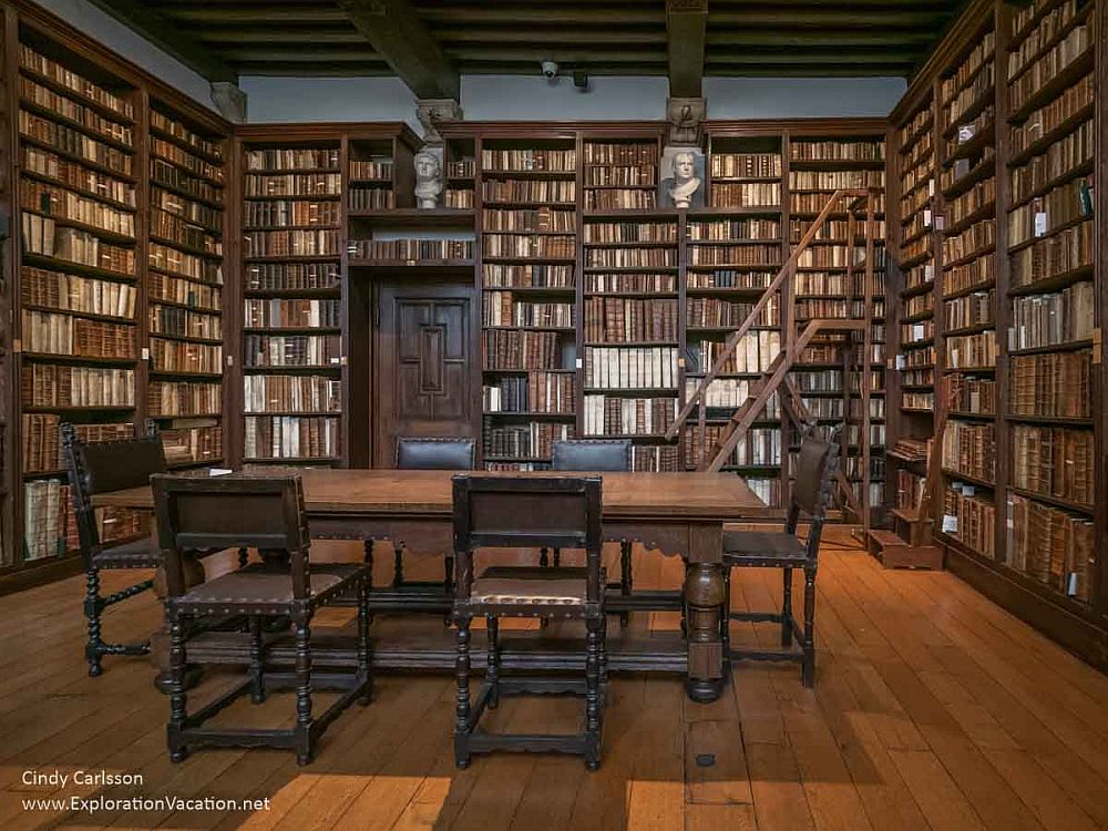 A library in the Plantin-Moretus Museum: a library with a large table in the middle with 4 chairs around it. The walls are covered, floor to almost the ceiling, with bookshelves filled entirely with books. A rolling ladder allowed people to reach the upper shelves.