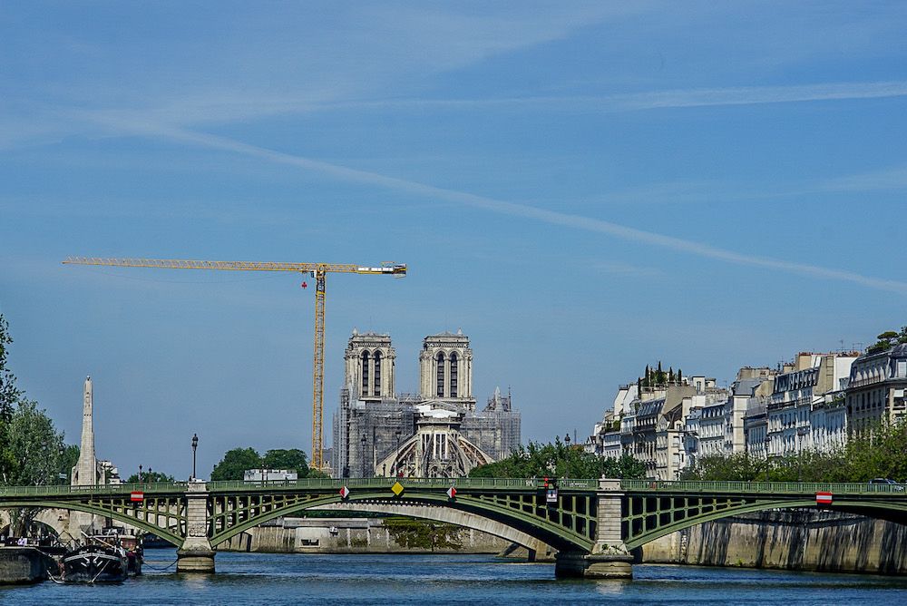A view on the Seine, with a bridge crossing it ahead, and beyond that, the Notre Dame Cathedral. Along the one visible bank, a row of typical Paris apartment buildings with mansard roofs.
