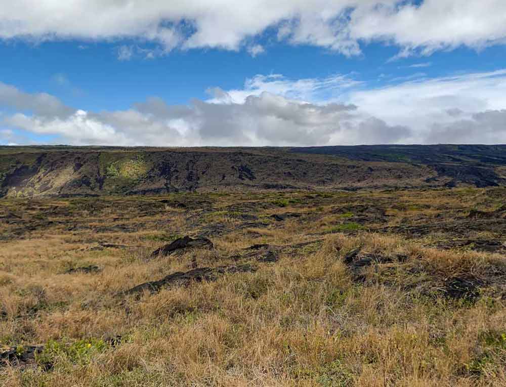 View across a grassy plain, with a crater in the distance at Hawaii Volcanoes National Park