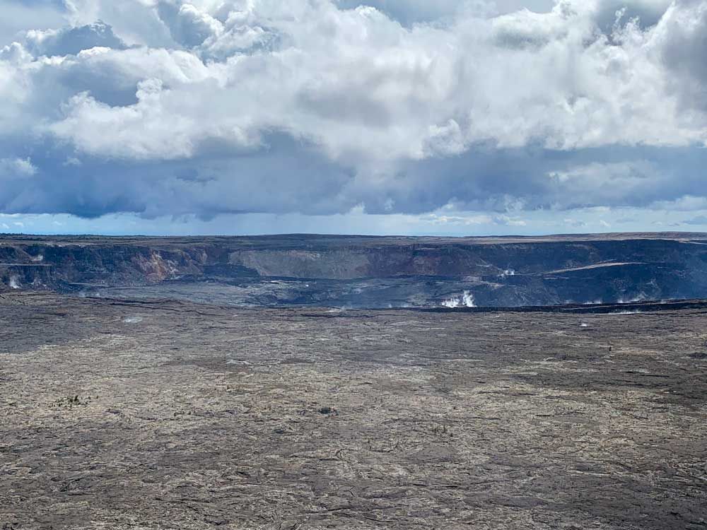 A wide crater reaches past the edges of the photo, gray sides inside, with a couple of wisps of steam at Hawaii Volcanoes National Park