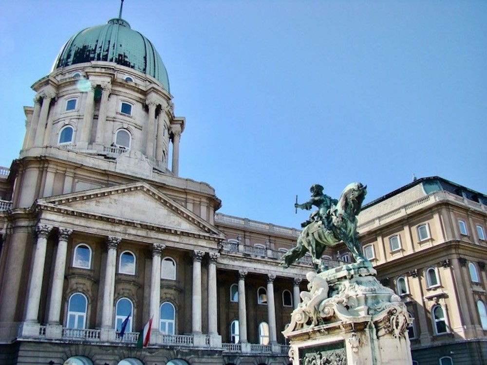 A grand building, with pillars across its entrance and a dome in its center, with a statue in front.