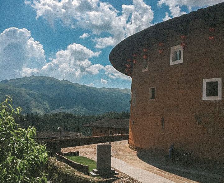 The side of a round Tulou, with mountains in the distance.