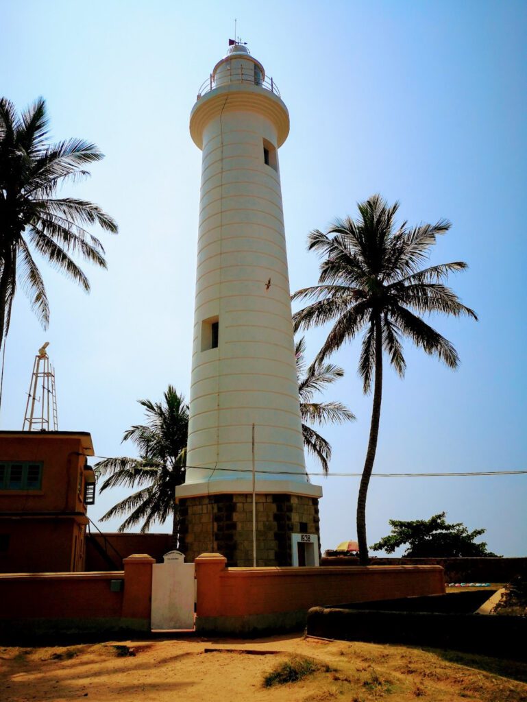 The white lighthouse at Galle Fort: round and tall, with palm trees around it.