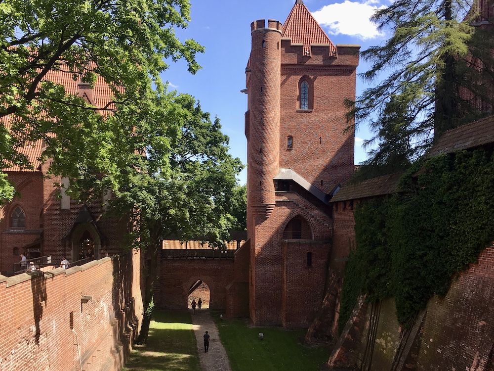 A tall tower of Malbork Castle: square red brick, with a pointed roof.