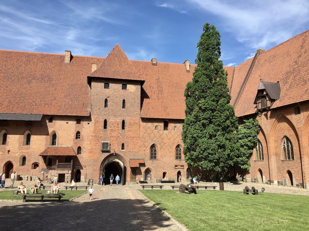 Two sides of Malbork Castle: several stories high in plain red brick, with some inset Romanesque arches.
