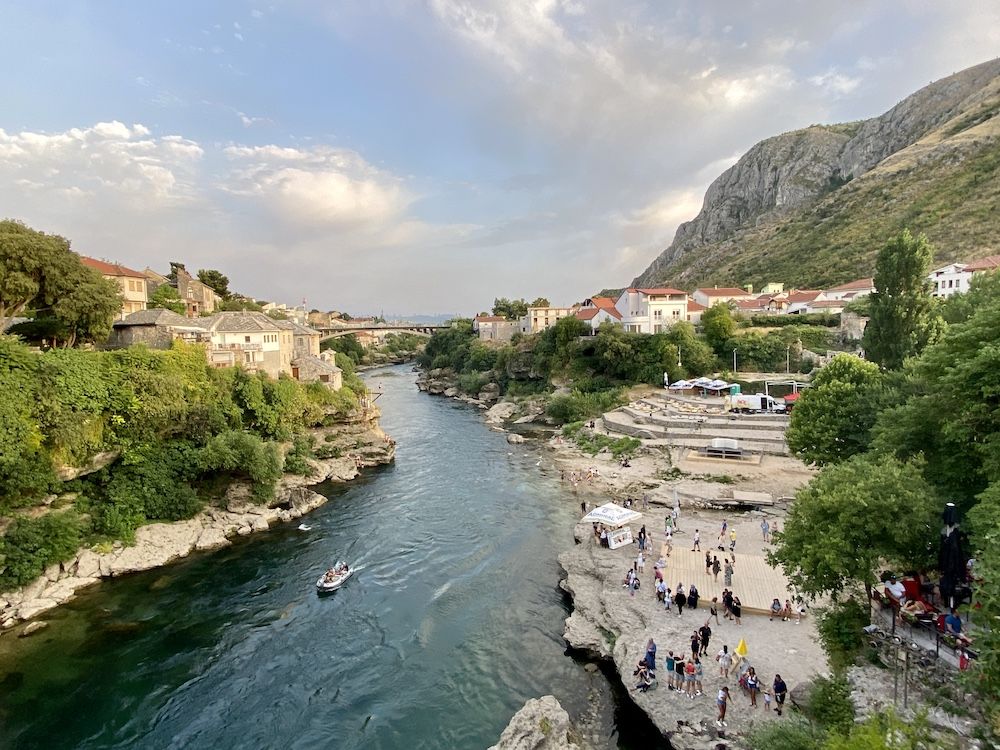 A view of Mostar from downriver: a small town along the river, with a mountain rising on one side.