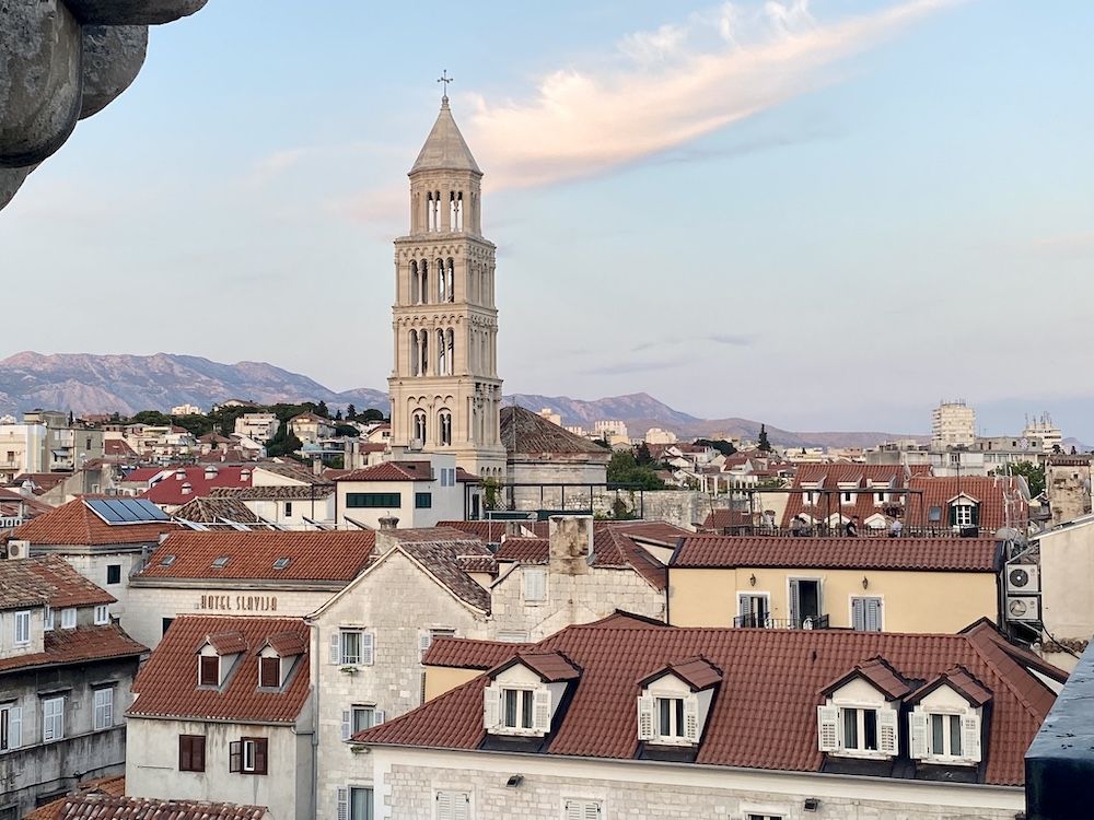 View over the old city of Split: low buildings with red roofs, one tall white tower.