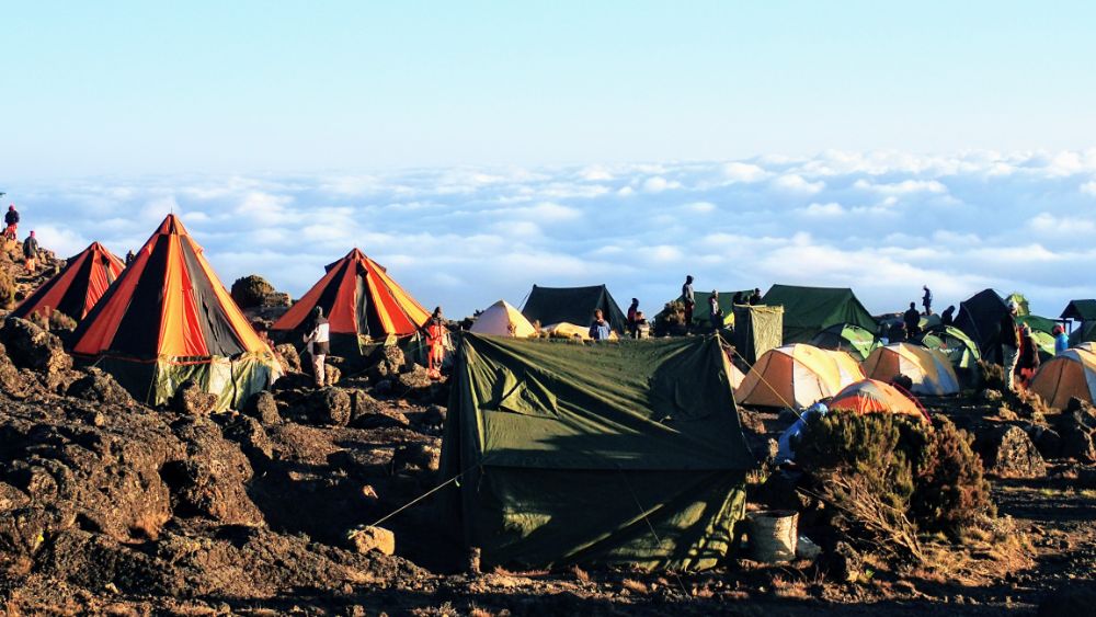 A cluster of tents. Behind them a view over the clouds.