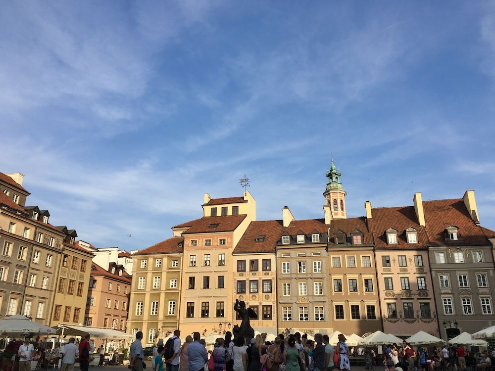 A row of buildings on a Warsaw market square. All are quite simple, with peaked roofs, 4-6 stories high, and painted in shades of brown and beige.