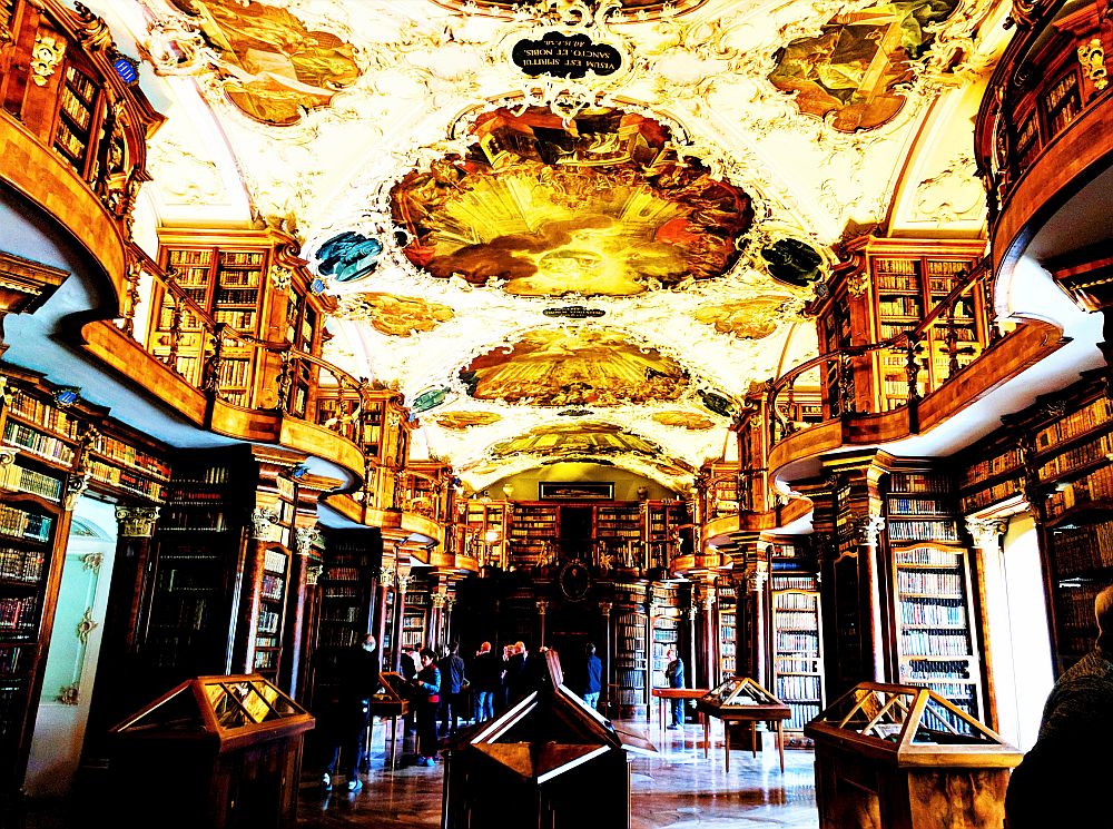 Library interior with orate painted ceiling and two floors of shelves full of books.