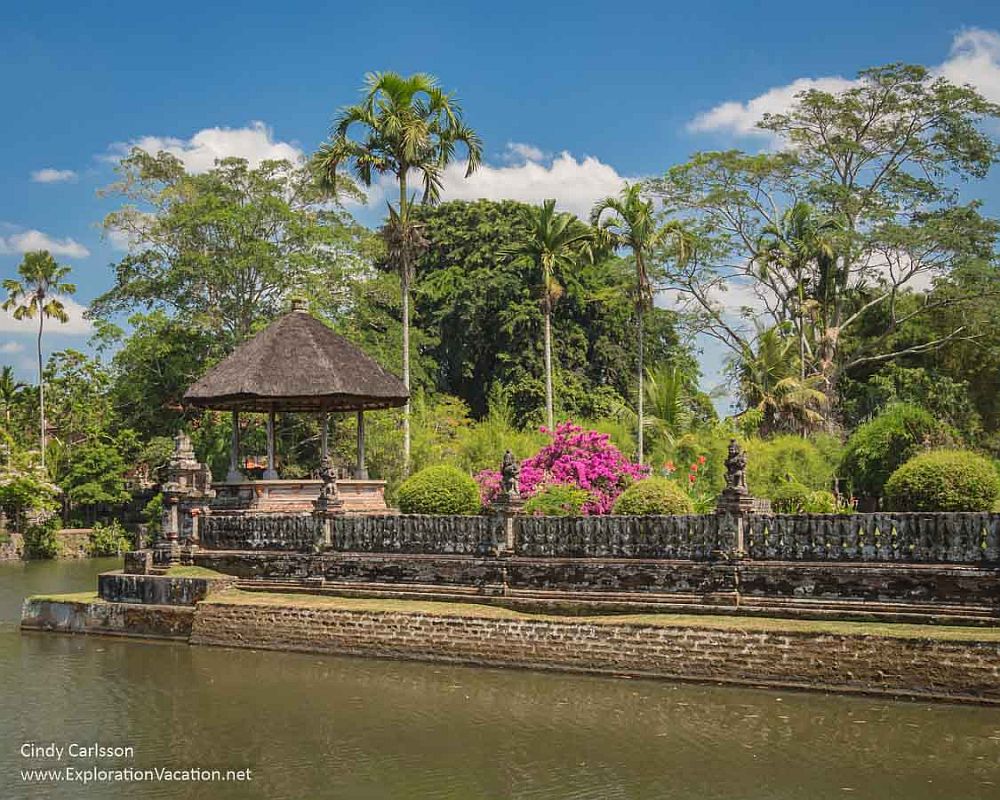 A garden with a balustrade along a lake, palm trees, and brightly-flowered shrubbery.