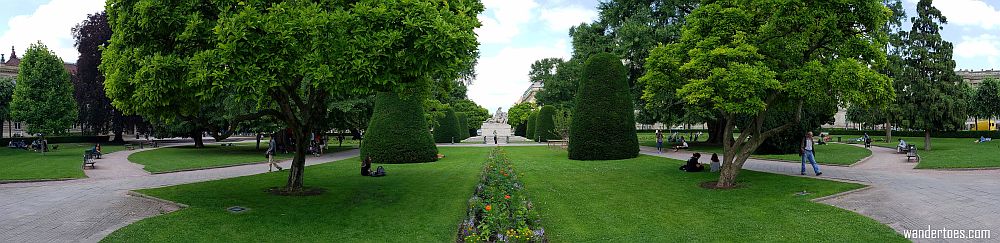 A symmetrical area with neat patches of grass, trees, paths and flower beds.