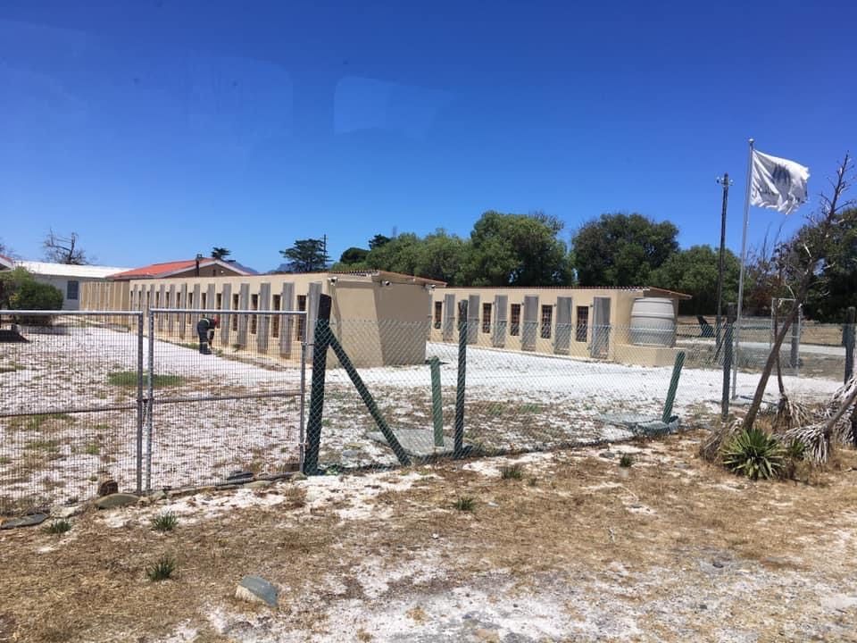 Two single-story wings of a building behind fencing: former cell blocks.