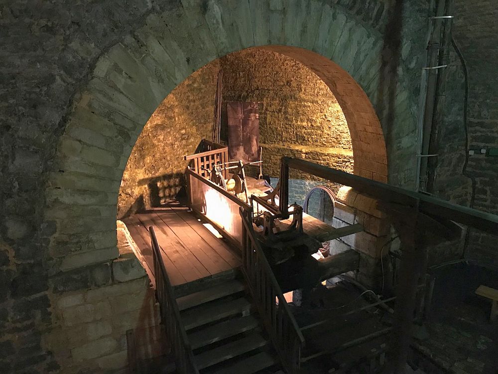 Indoors, looking through an archway to a wooden platform with some machinery on it.