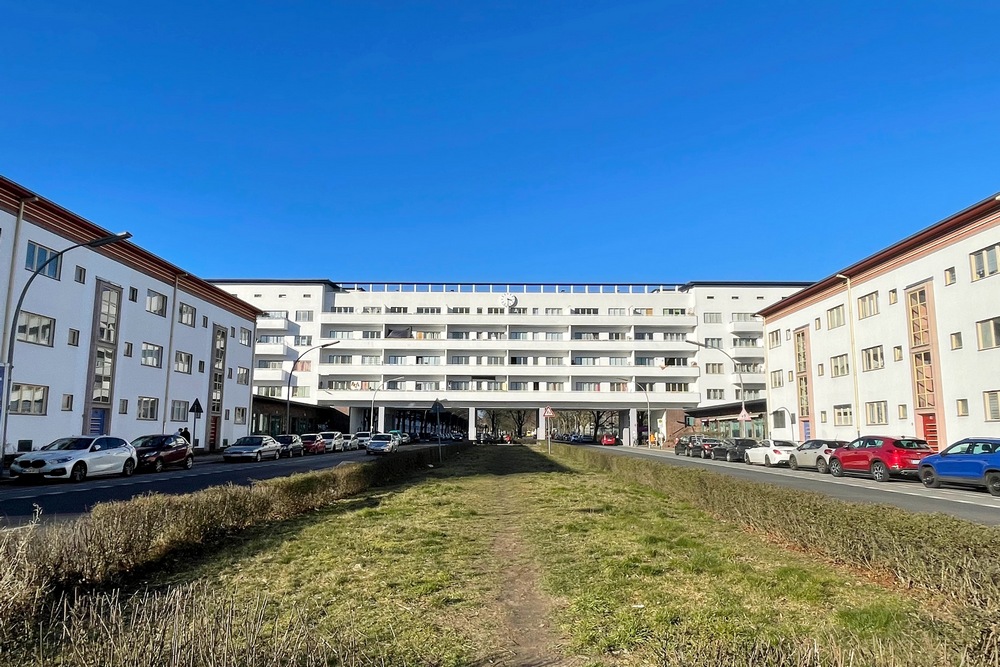 A very wide, white building with 4 stories of apartments and two lanes of roads passing through the ground floor.