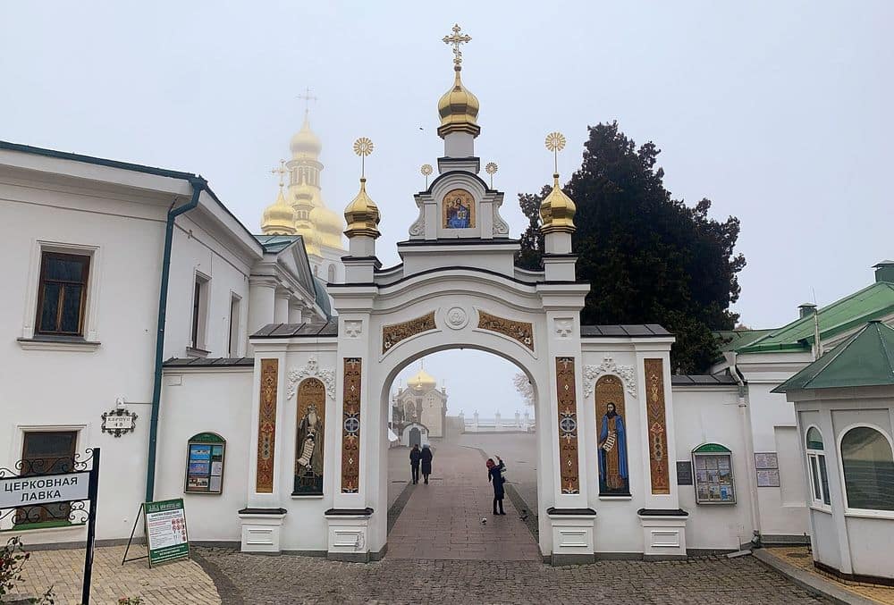 An ornate gateway in white with painted images in each panel and gold dome above it.