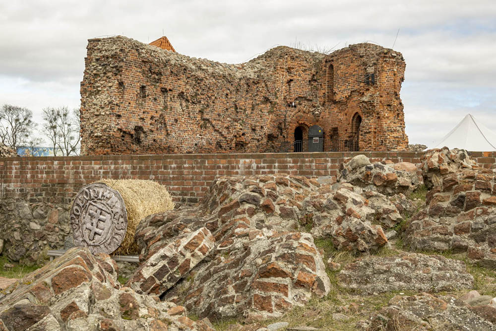 The deteriorated hulk of a castle made of bricks, with lots of fallen bricks on the ground in front of it.